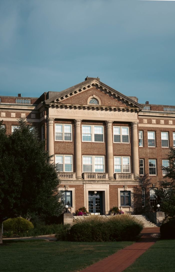 A grand historic building with elegant columns and a spacious front lawn, captured in daylight.